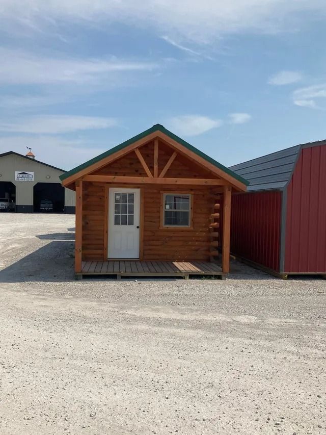 A small wooden cabin with a green roof is sitting in a gravel lot.