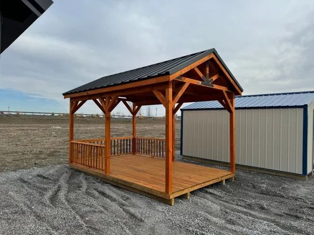 A wooden gazebo with a black roof is sitting on top of a dirt field.