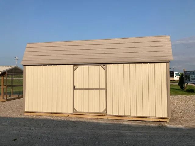 A tan shed with a door is sitting on the side of the road.