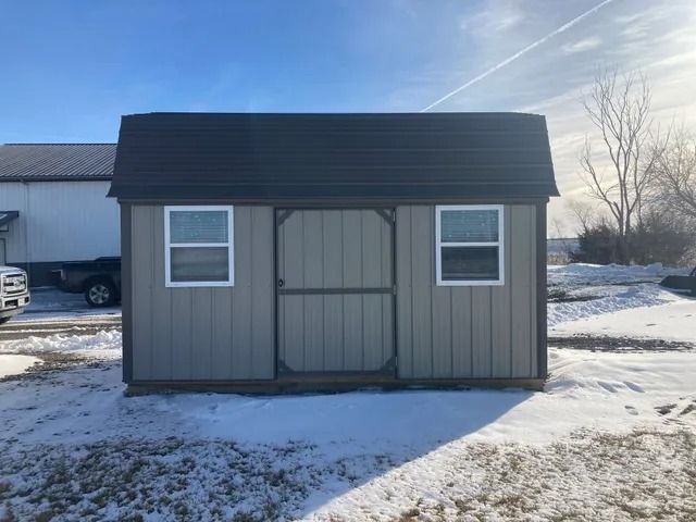 A shed with a black roof is sitting in the snow.