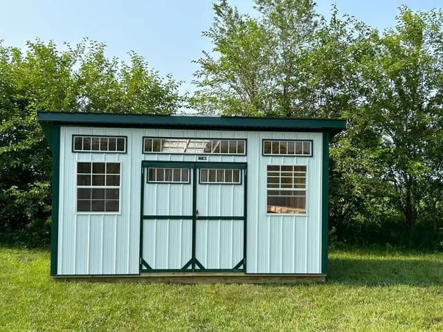 A white and green shed is sitting in the middle of a grassy field.