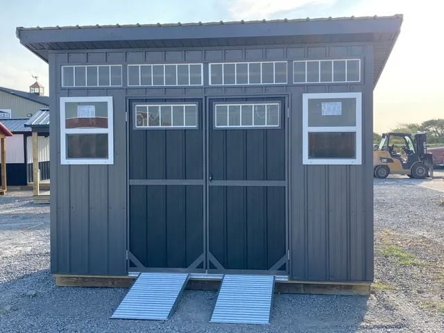 A gray shed with a forklift parked in front of it.
