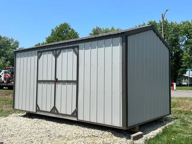 A small metal shed is sitting on top of a gravel lot.
