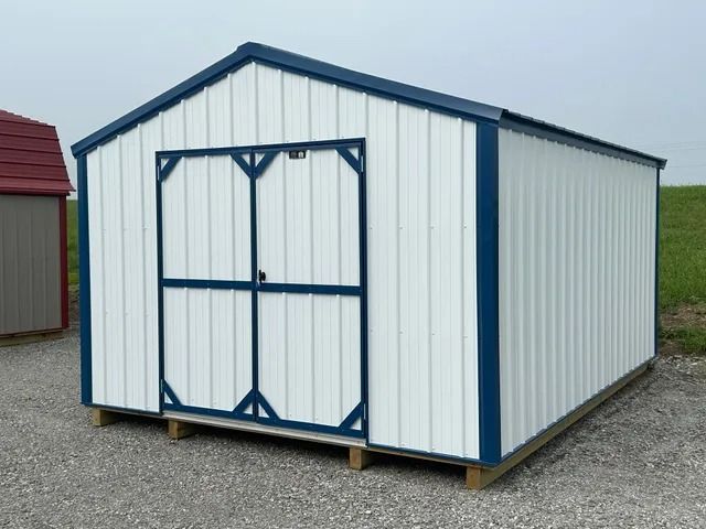 A white shed with blue trim is sitting on top of a gravel road.