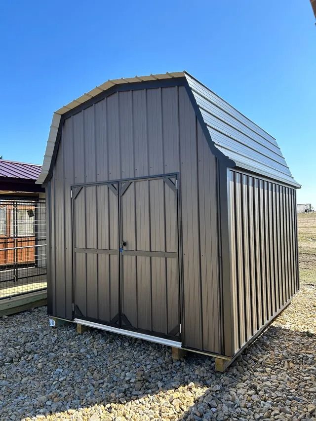 A brown barn shed is sitting on top of a gravel lot.