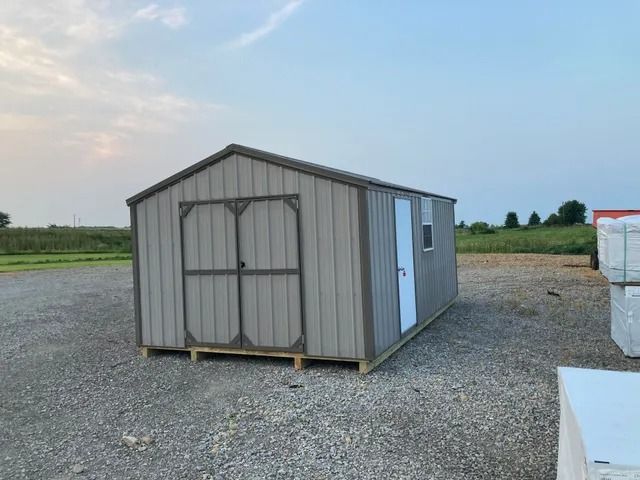 A small shed is sitting in the middle of a gravel lot.