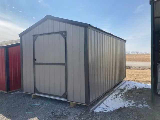 A small metal shed with a door is sitting on top of a gravel lot.