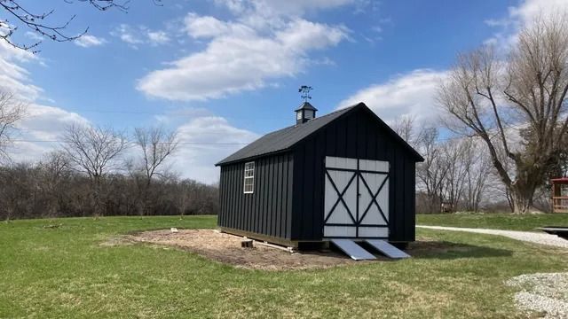 A black shed with a white door is sitting in the middle of a grassy field.