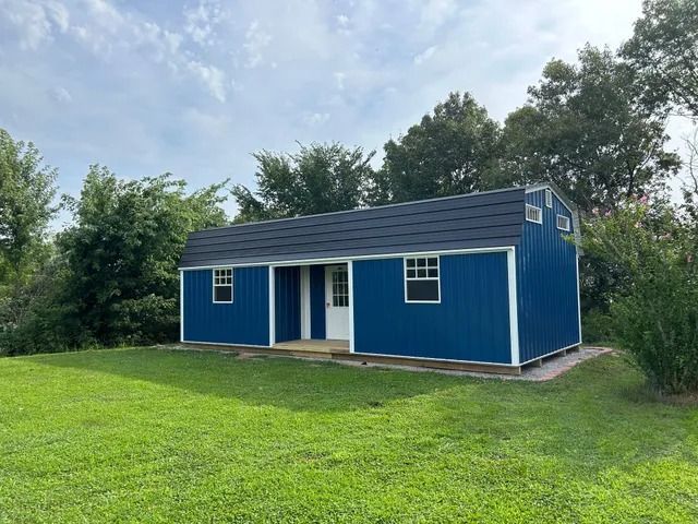 A blue and white shed is sitting in the middle of a lush green field.