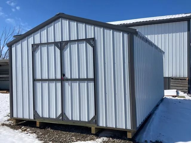 A white metal shed is sitting in the snow in front of a building.