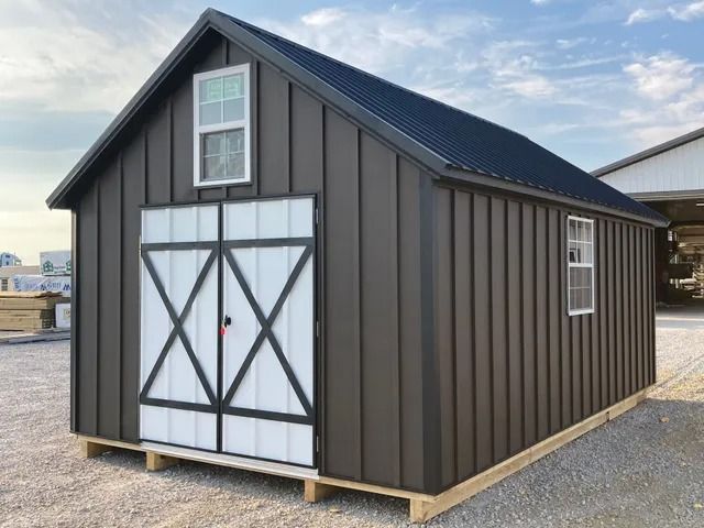 A black shed with white doors and windows is sitting on a wooden pallet.