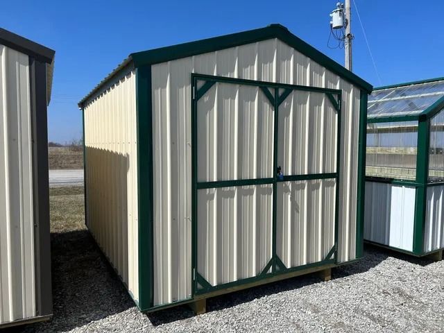 A white shed with green trim is sitting on top of a gravel lot.