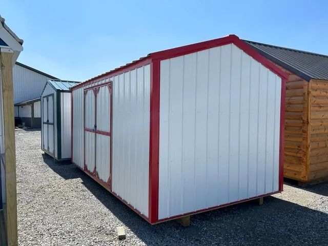A white shed with a red trim is sitting in a gravel lot.