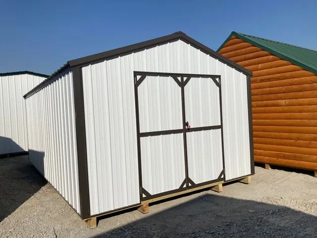 A white shed with a brown trim is sitting next to a wooden shed.