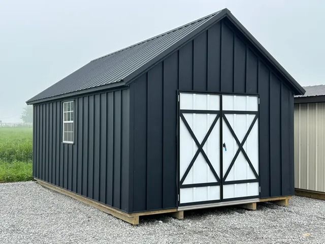 A black shed with white doors and windows is sitting on top of a gravel lot.