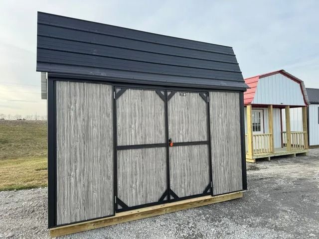 A shed with a black roof is sitting in a dirt field.