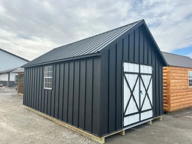 A black shed with a white door is sitting on a wooden platform.