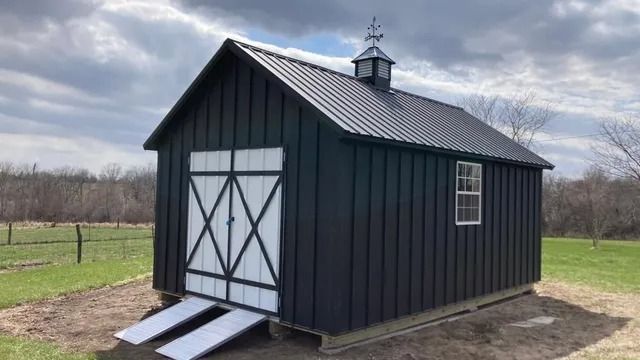 A black barn with white doors is sitting in the middle of a grassy field.