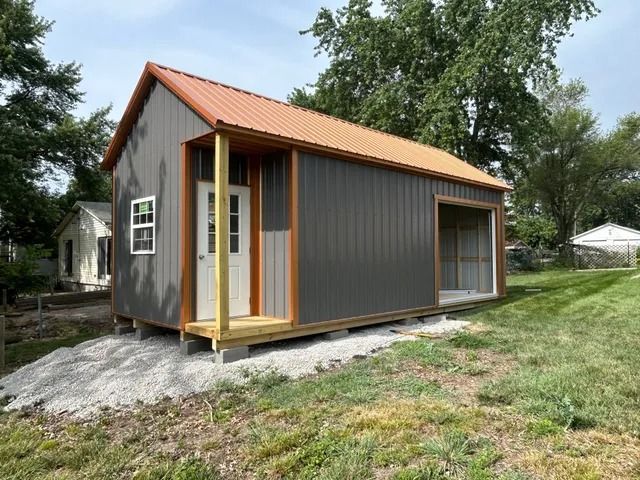 A small house with a porch and a garage is sitting in the middle of a grassy field.