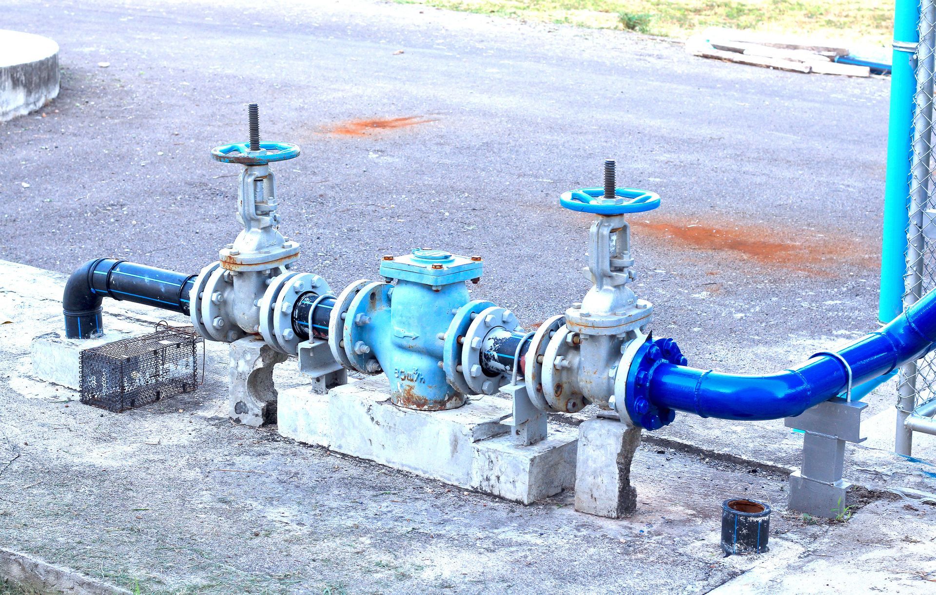Blue and gray water pipes with valves and a central pump, set on concrete blocks.