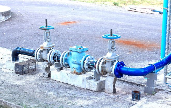 Blue and gray water pipes with valves and a central pump, set on concrete blocks.