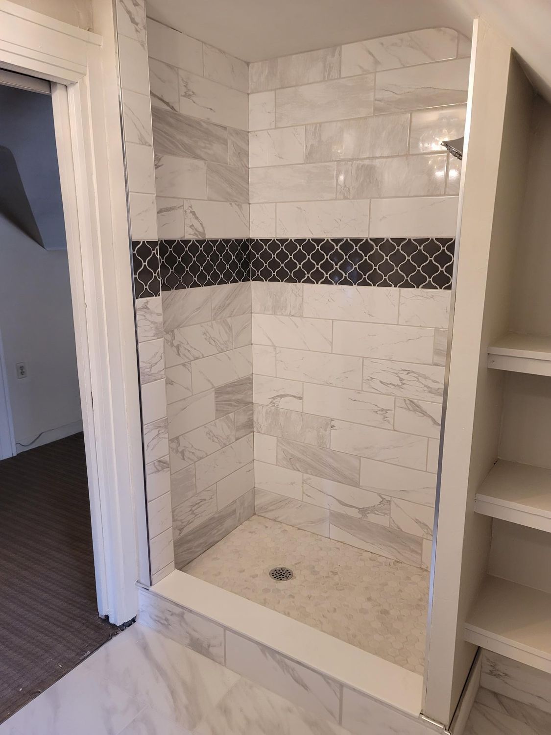 Tiled shower with marble-look walls and decorative dark border. Built-in shelves to the right.