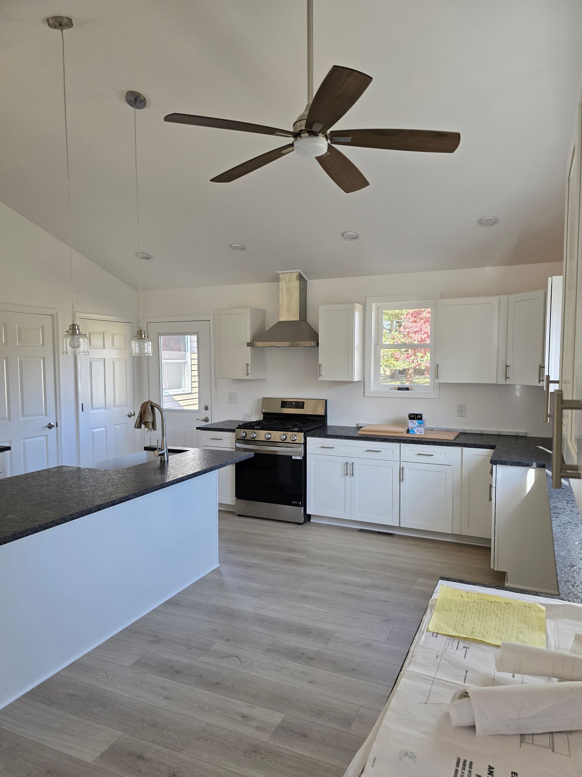 Modern kitchen with white cabinets, dark countertops, and gray flooring. Stainless steel range and hood.