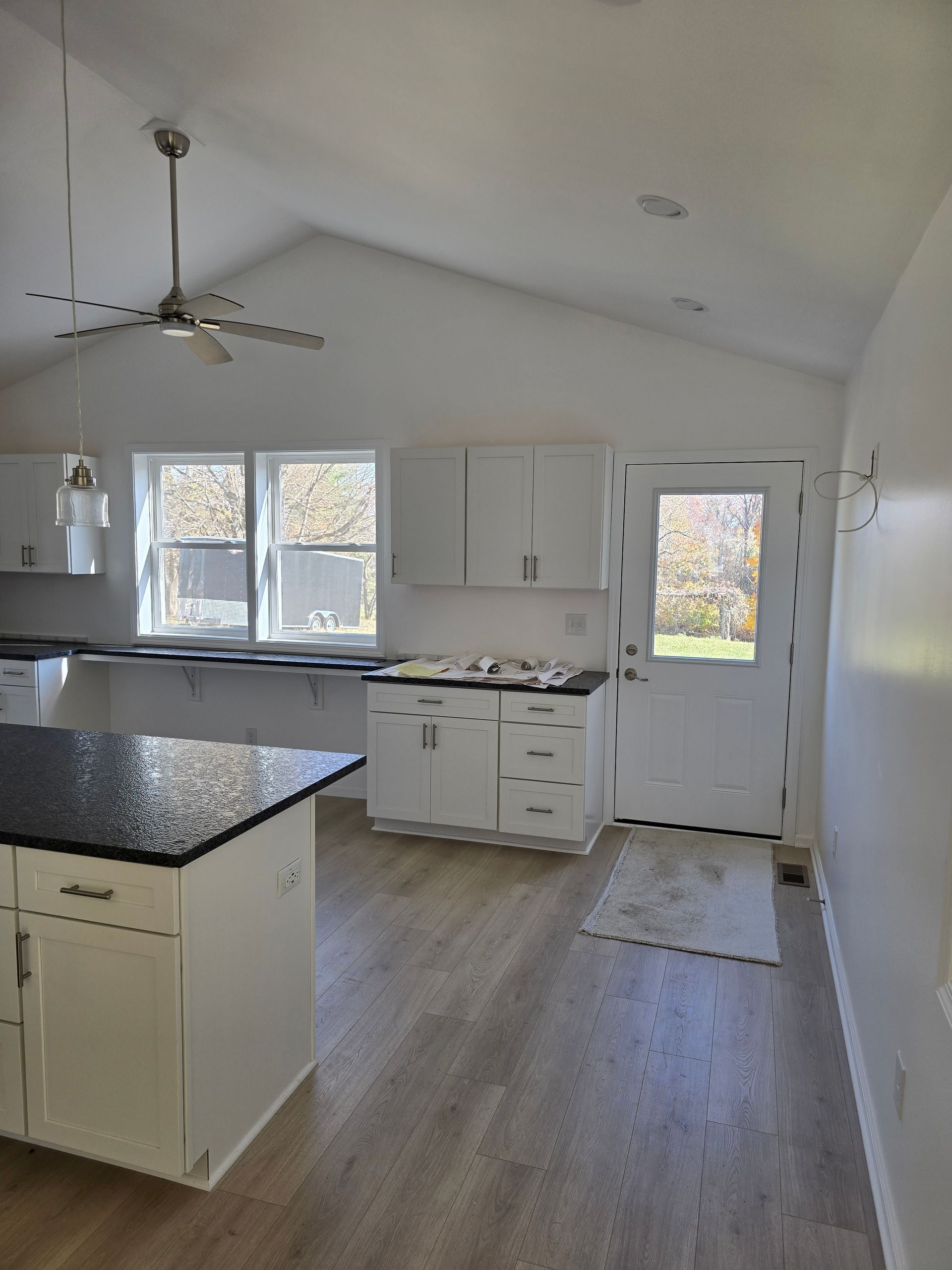 White kitchen with island, cabinets, door, windows, and light gray flooring.