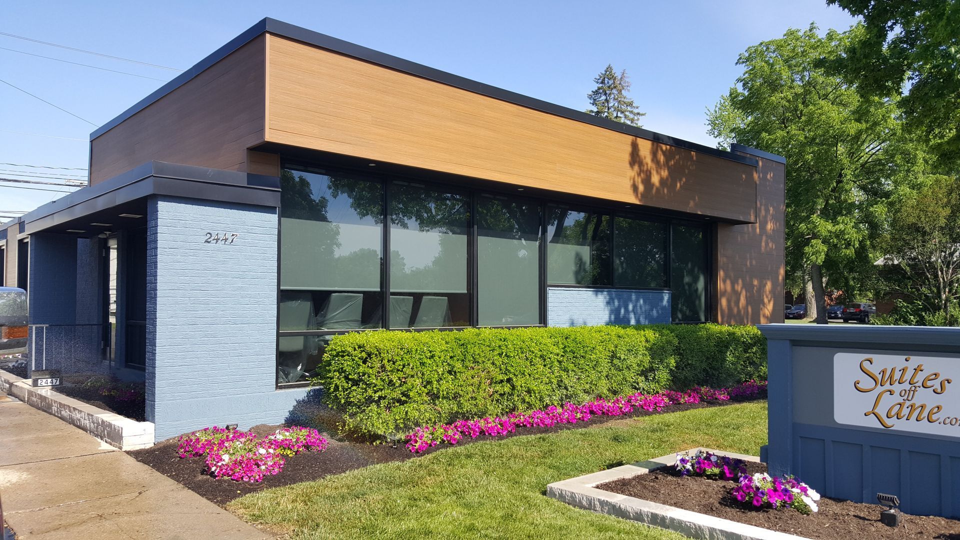 Office building with dark windows, brick facade, and trimmed bushes in front. Sign reads 