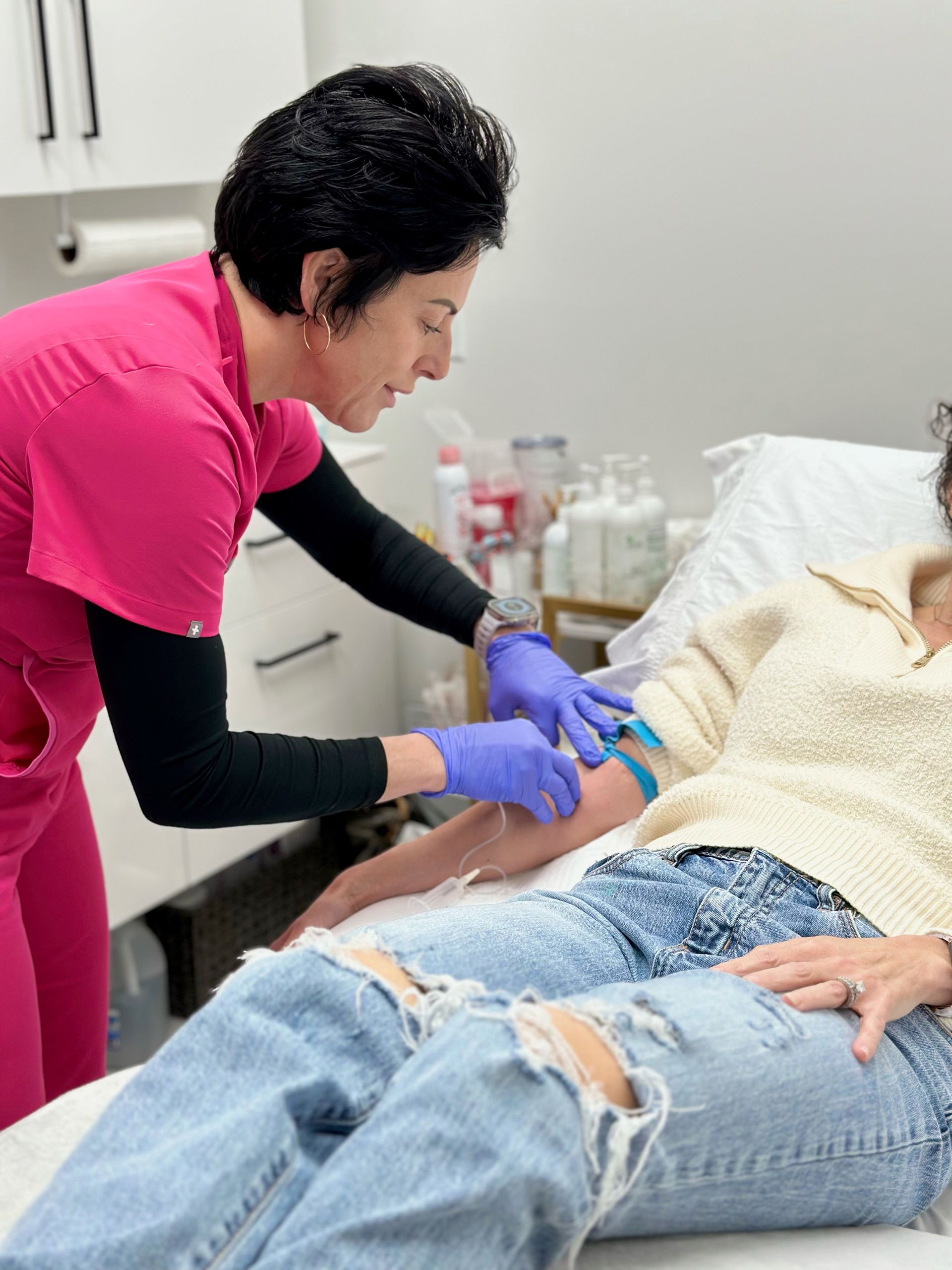 a woman in a pink scrub injecting a woman patient