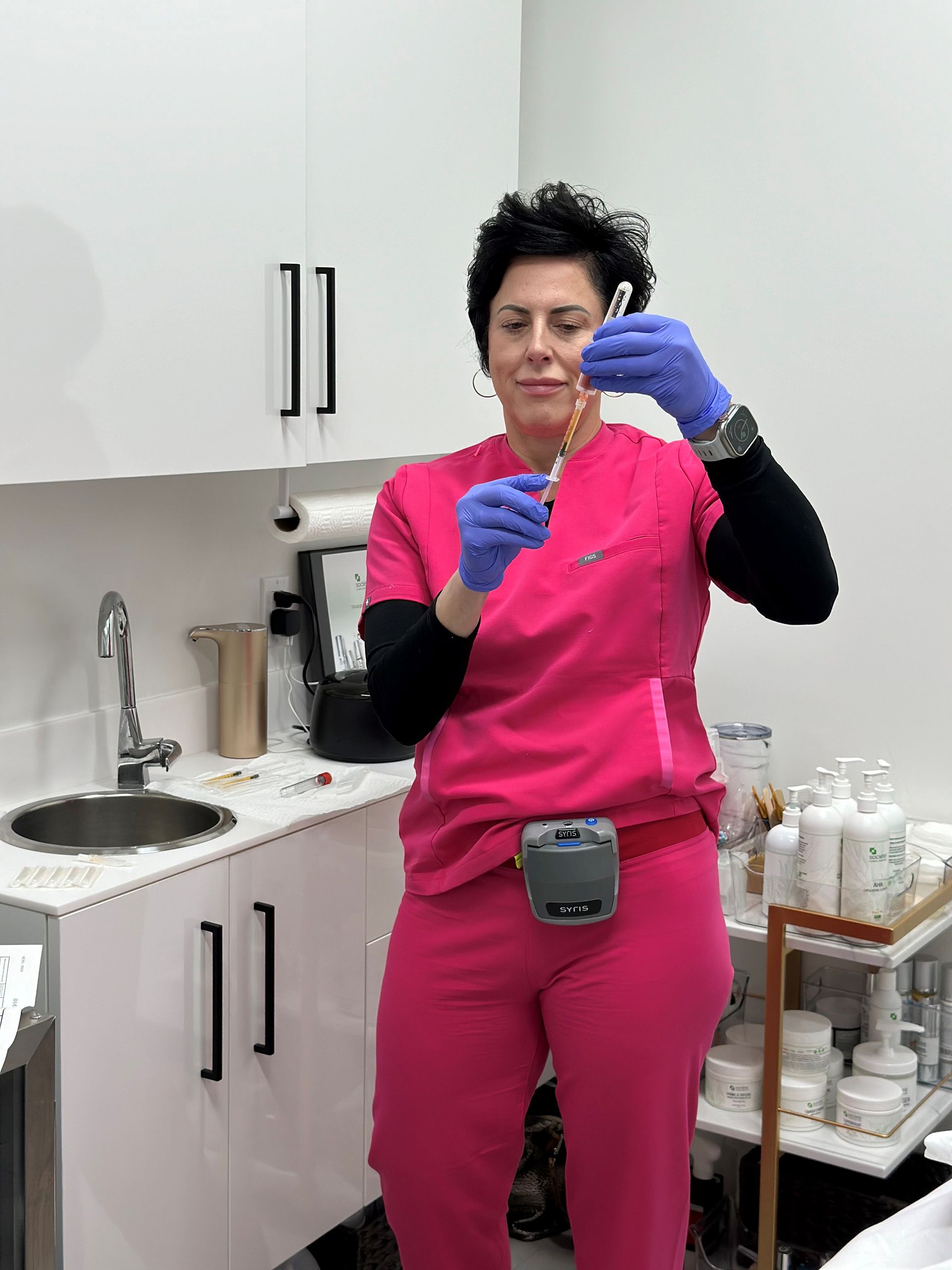 a woman in pink scrubs is holding a syringe in a kitchen .