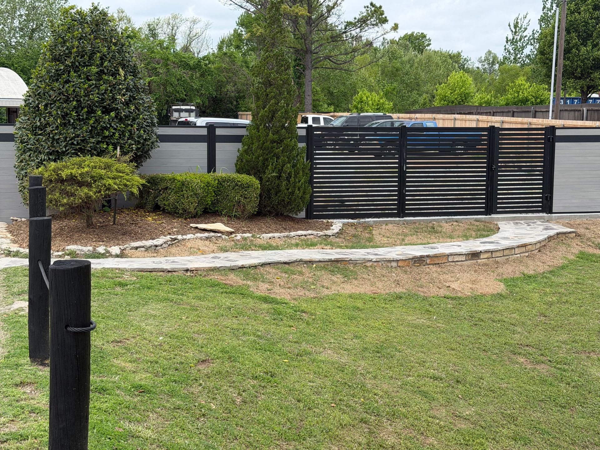 Residential driveway with black gate, manicured shrubs, and a grassy front yard.