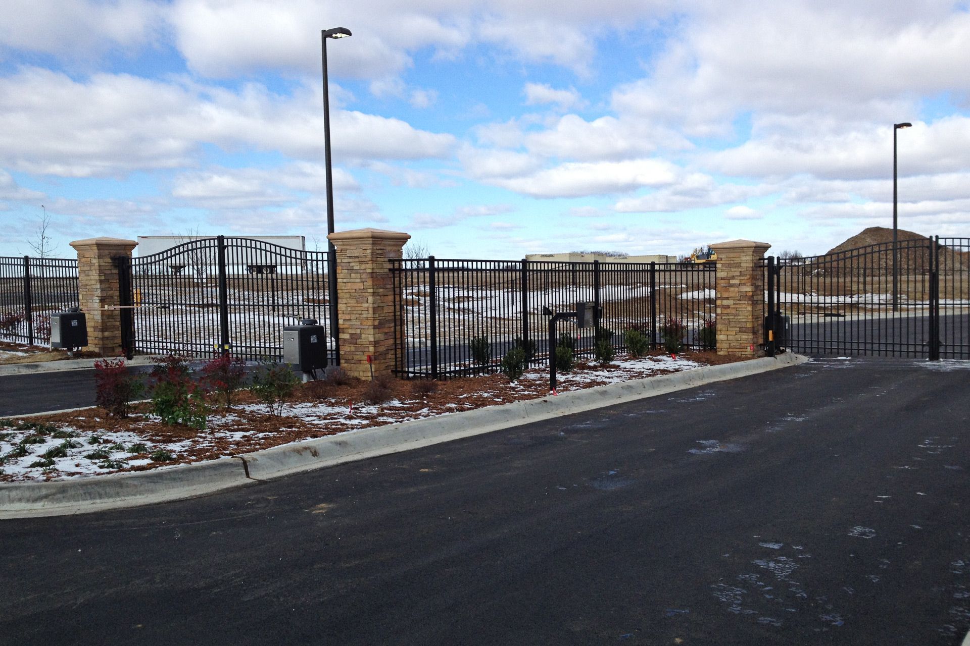 Gated entrance with brick columns and black metal fence on a cloudy day.