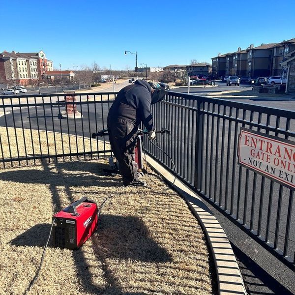 Person welding metal fence, generator nearby, in front of an apartment complex. 