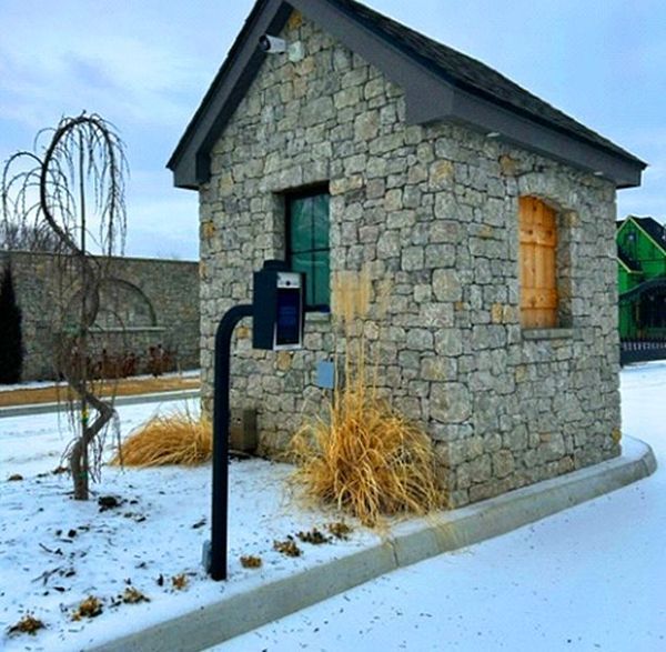 Stone guardhouse with a small window, brown door, and access system in a snow-covered area.