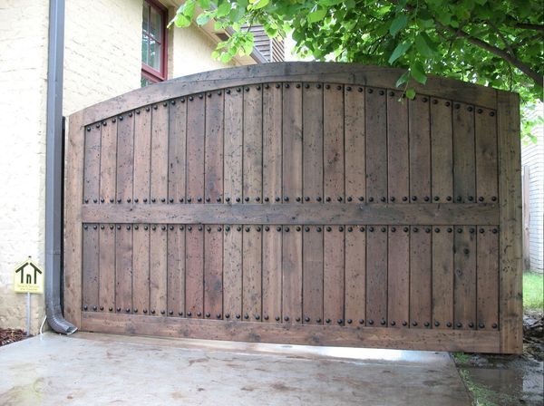 Wooden arched gate with vertical planks, secured by horizontal beams and rivets.