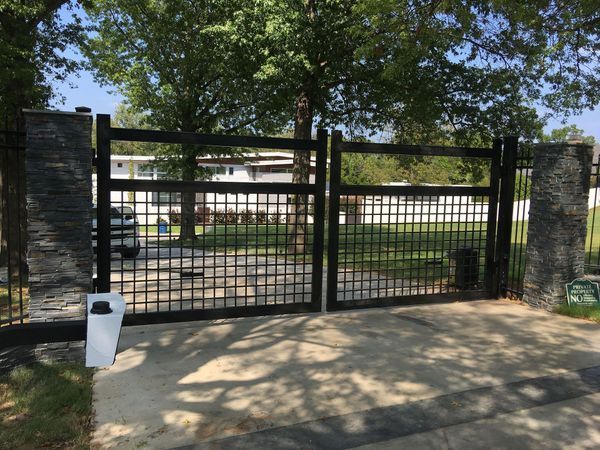 Black metal gate with stacked stone columns, driveway in front of a house.