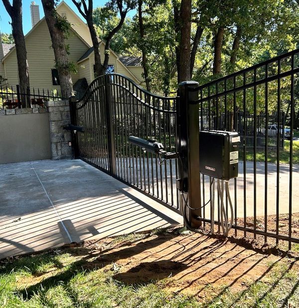 Black metal driveway gate, automatic opener, set in a yard.