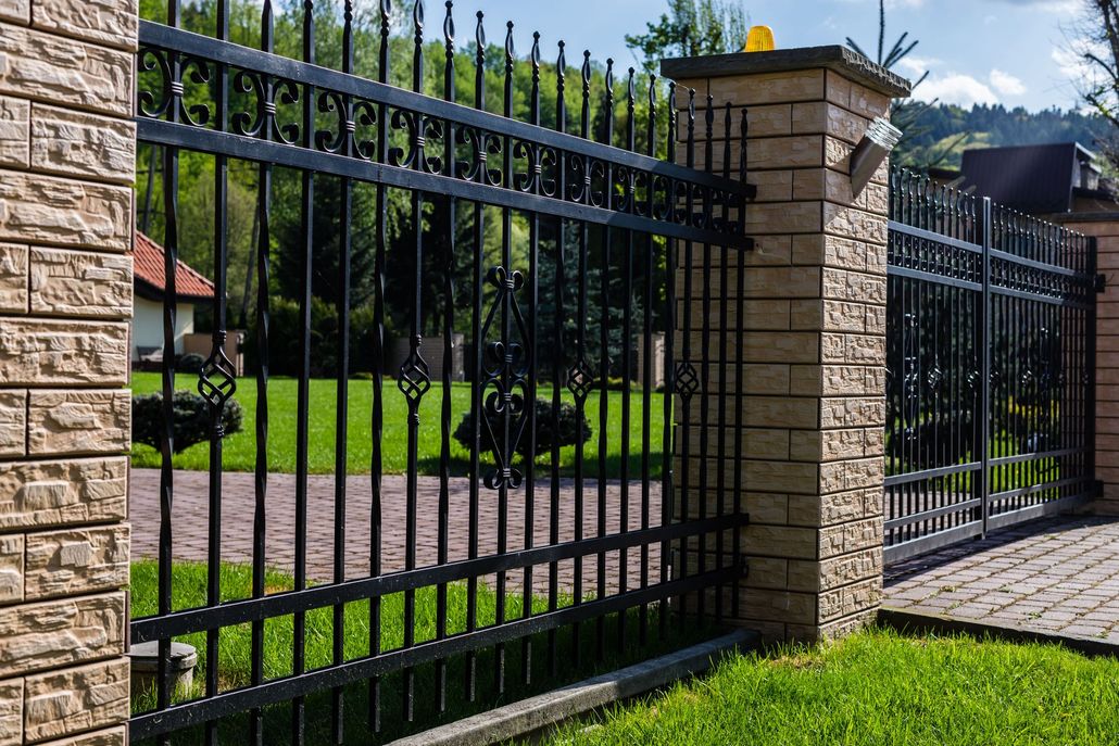 Black metal fence with stone pillars on green grass.