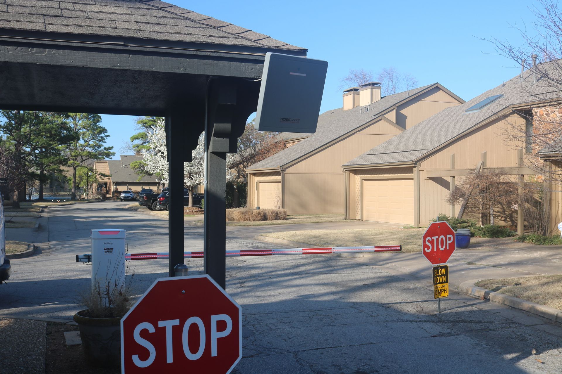A gated community entrance with a red-and-white striped barrier arm, two red stop signs, and a security access reader.