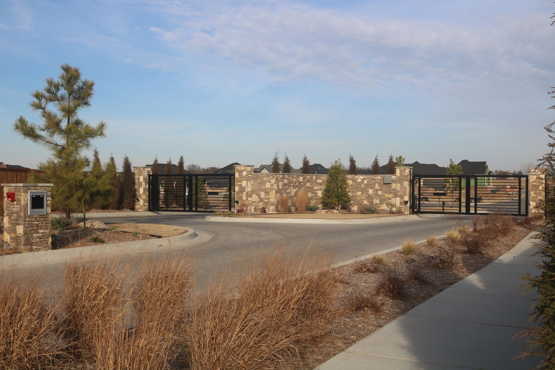 Stone-pillared entrance gate to a residential community with paved roads and landscaping under a clear sky.