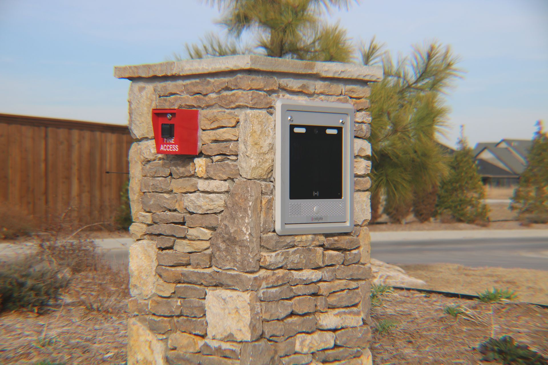 A stone pillar with a red fire alarm pull station and a silver entry intercom system mounted outdoors.