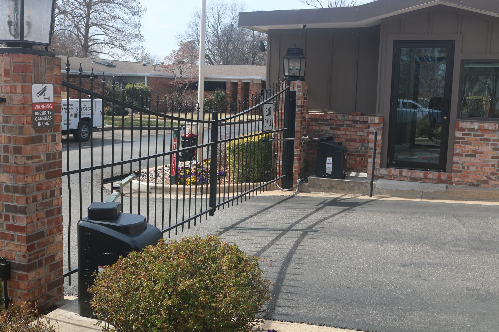 A brick-pillared security gate at the entrance to a residential complex on a sunny day.