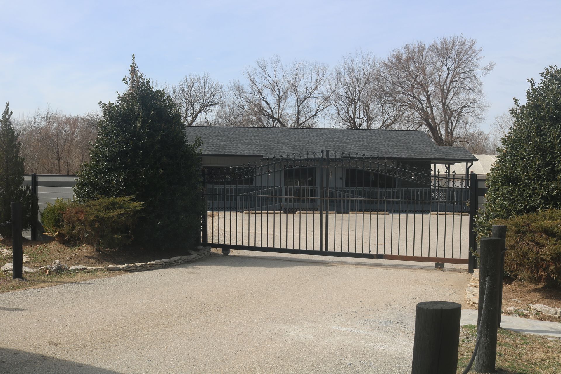 A grey, single-story commercial building sits behind a closed metal security gate on a gravel driveway.