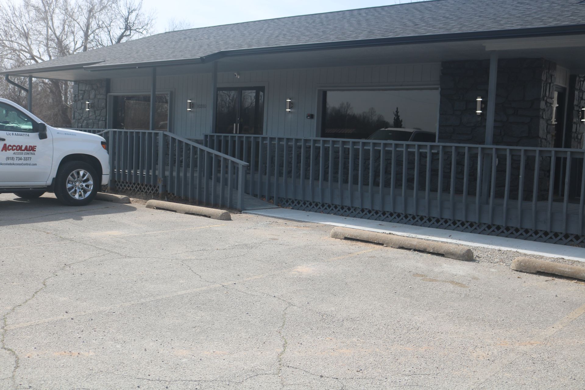 A white truck is parked in front of a grey building featuring a wide entrance ramp with grey railings.