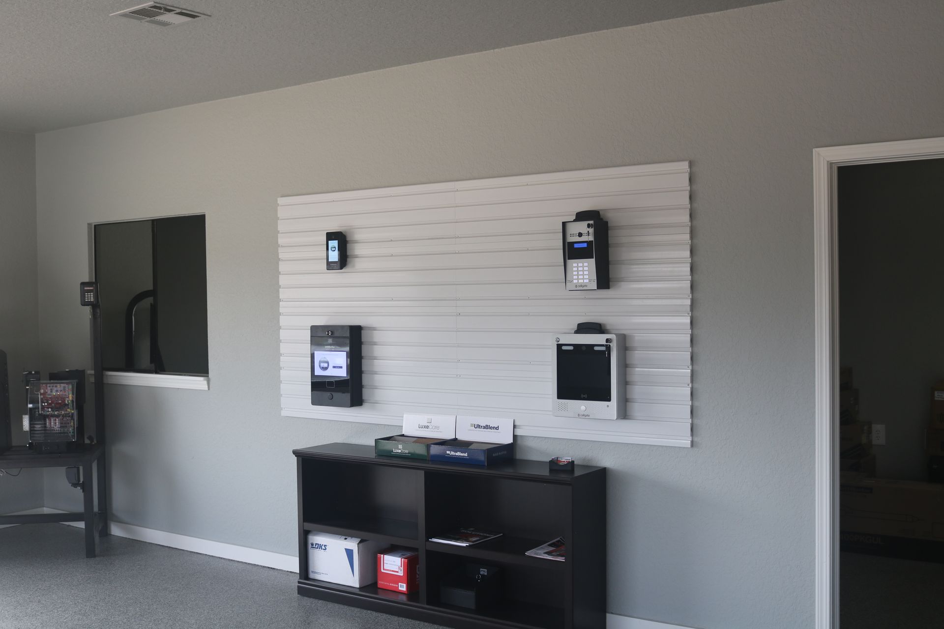 Four electronic wall panels mounted on a white slat board above a black shelving unit in a neutral-colored room.