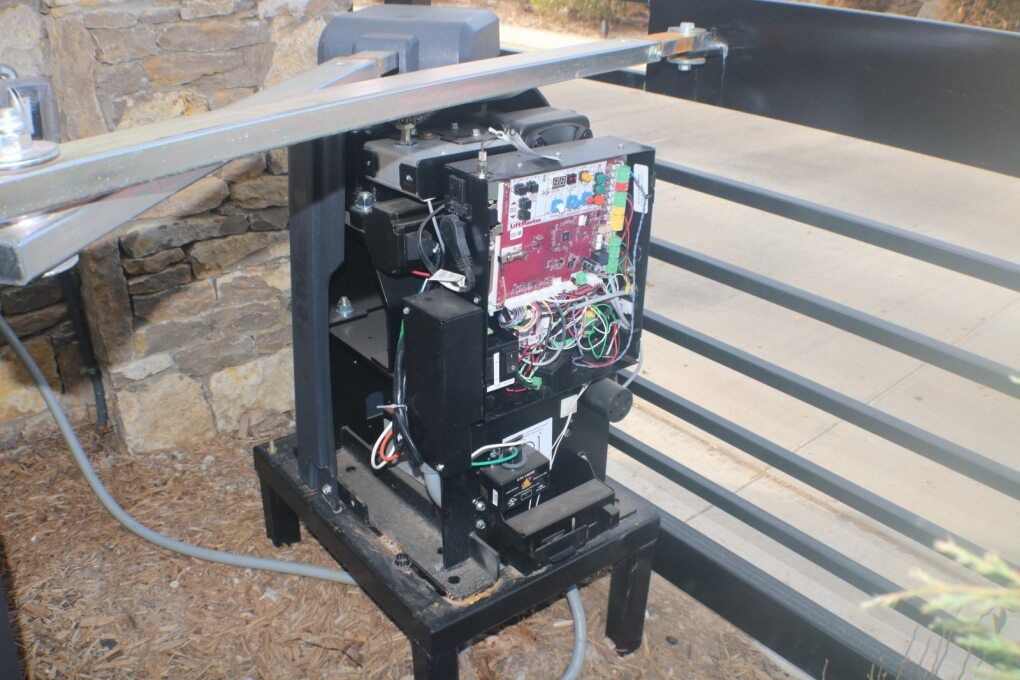Open-casing of a mechanical automatic gate operator motor with visible circuit board and wiring, installed outdoors.