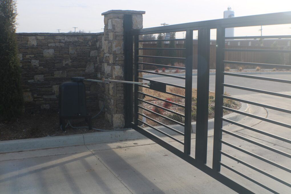 A black metal gate attached to a stone pillar, connected to a mechanical motor on a concrete surface.