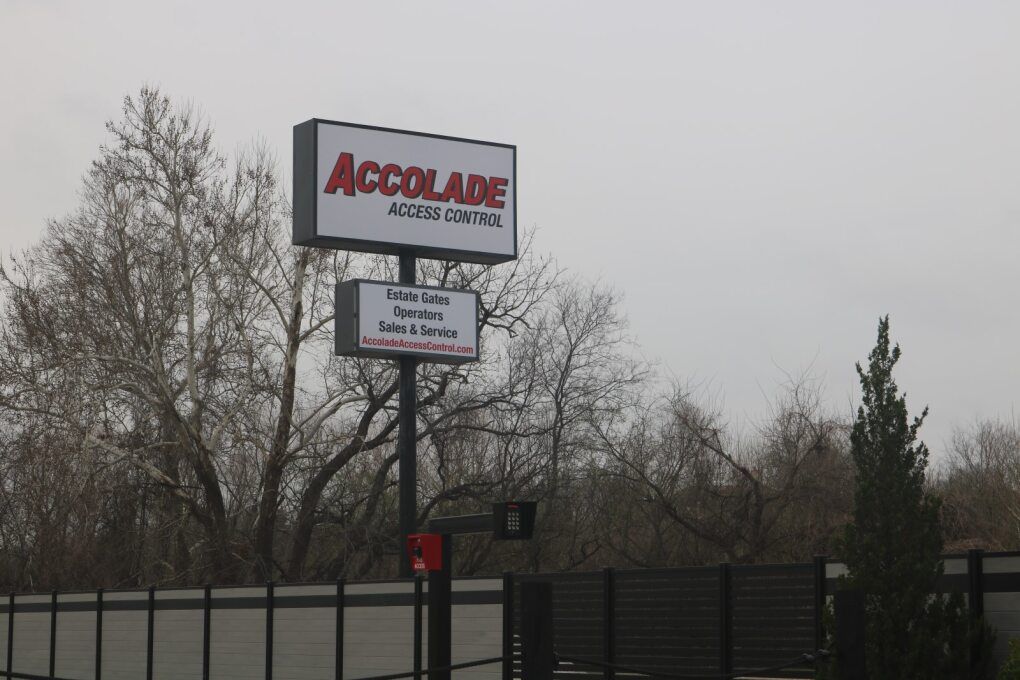 A two-tiered sign for Accolade Access Control on a metal pole against a cloudy sky and bare trees.