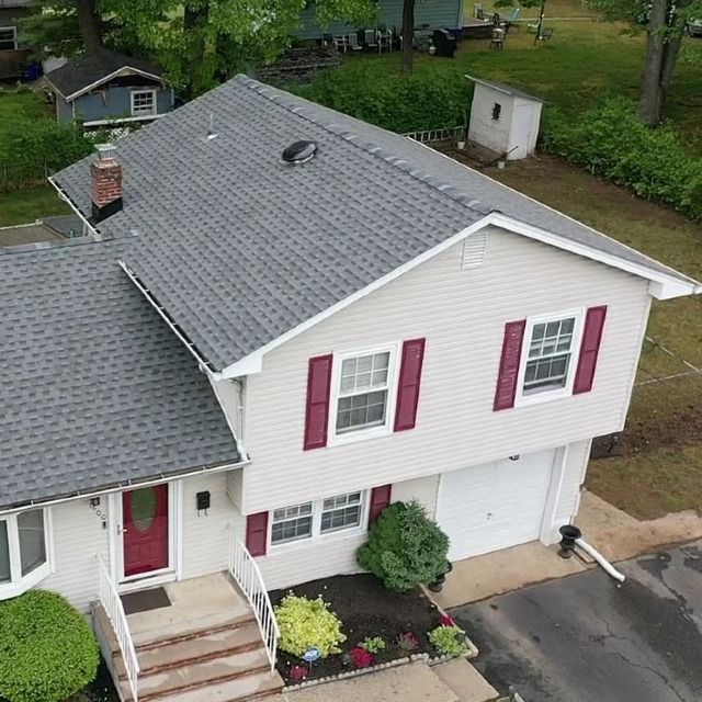 Two-story house with grey roof, cream siding, red shutters and door, and a small lawn with bushes.